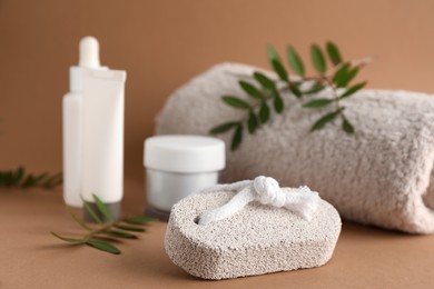 Pumice stone, cosmetic products and towel on brown background