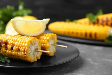 Plate of grilled corn cobs and lemon on grey table, closeup. Space for text