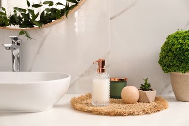 Photo of Soap dispenser, plants and candle near vessel sink in bathroom