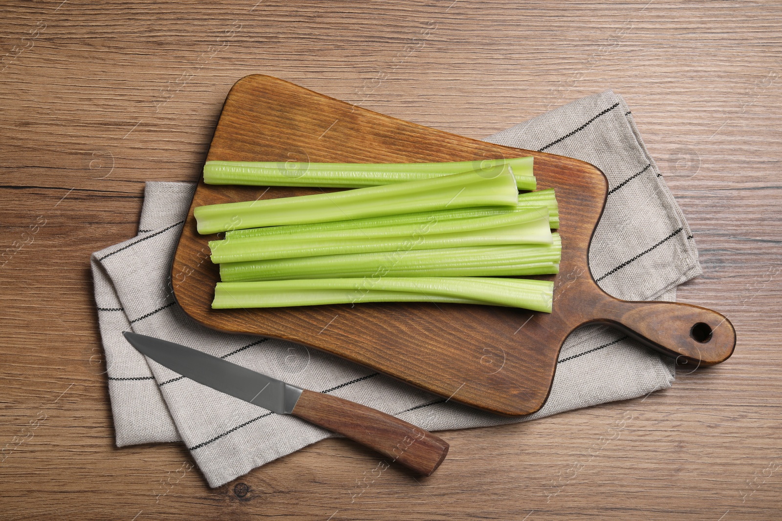 Photo of Board with fresh green celery and knife on wooden table, flat lay
