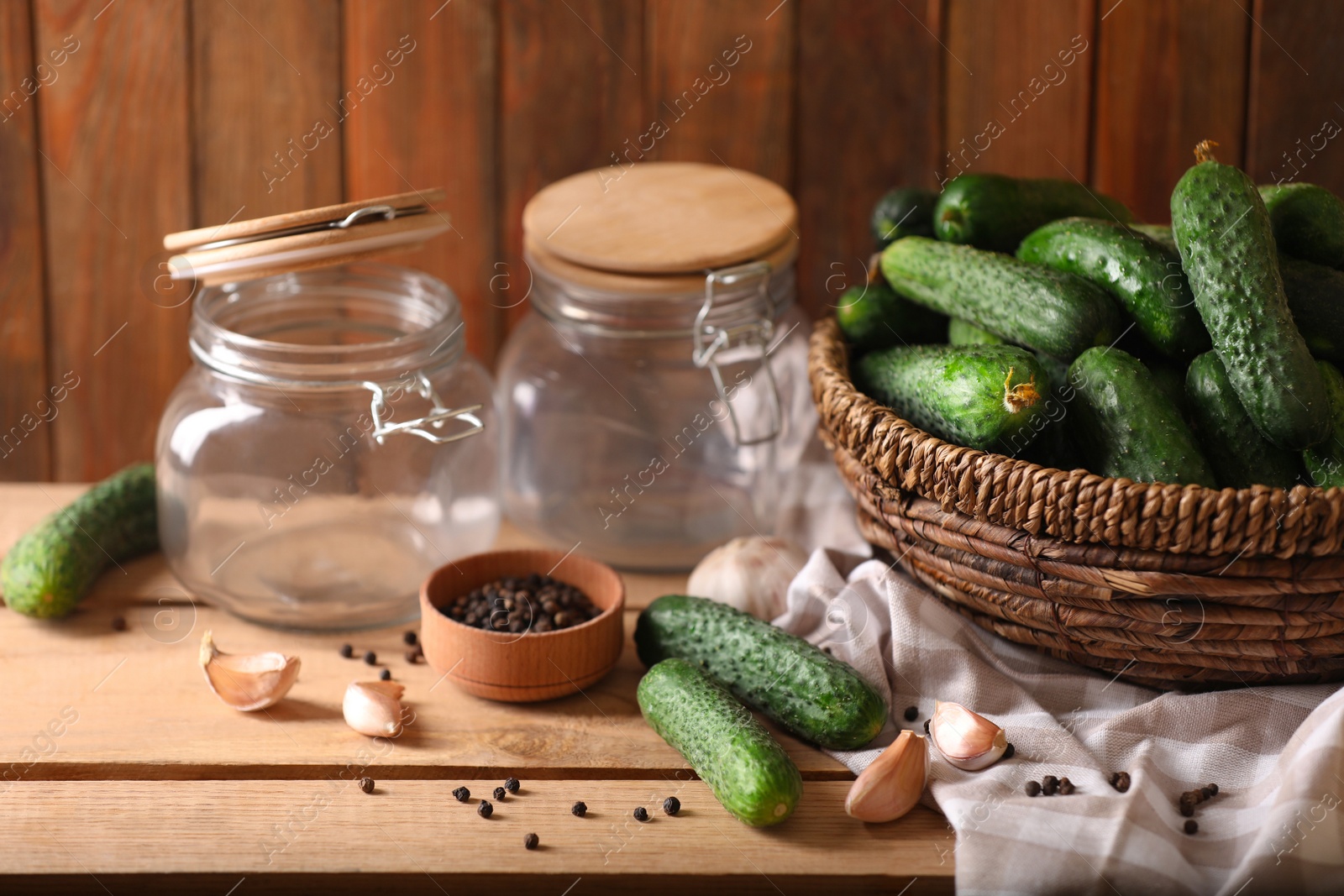 Photo of Fresh cucumbers and other ingredients near empty jars prepared for canning on wooden table