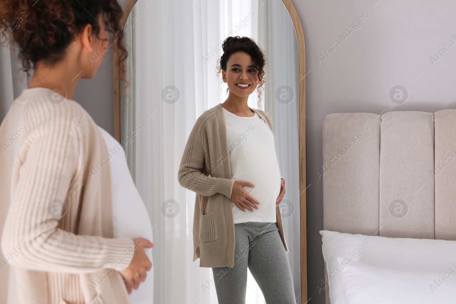 Photo of Pregnant young African-American woman near mirror at home