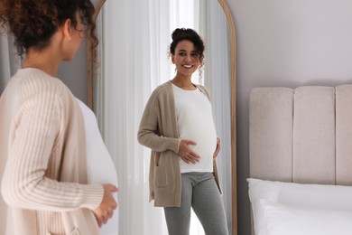 Pregnant young African-American woman near mirror at home