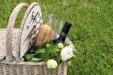 Picnic basket with wine, bread and flowers on green grass outdoors