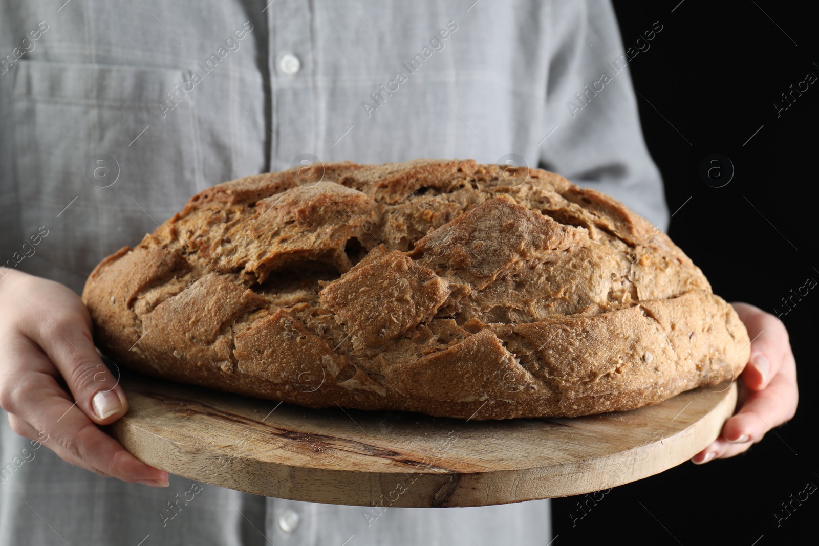 Photo of Woman holding freshly baked bread on black background, closeup