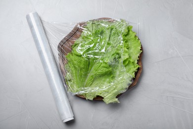 Photo of Fresh lettuce with plastic food wrap on light grey table, flat lay