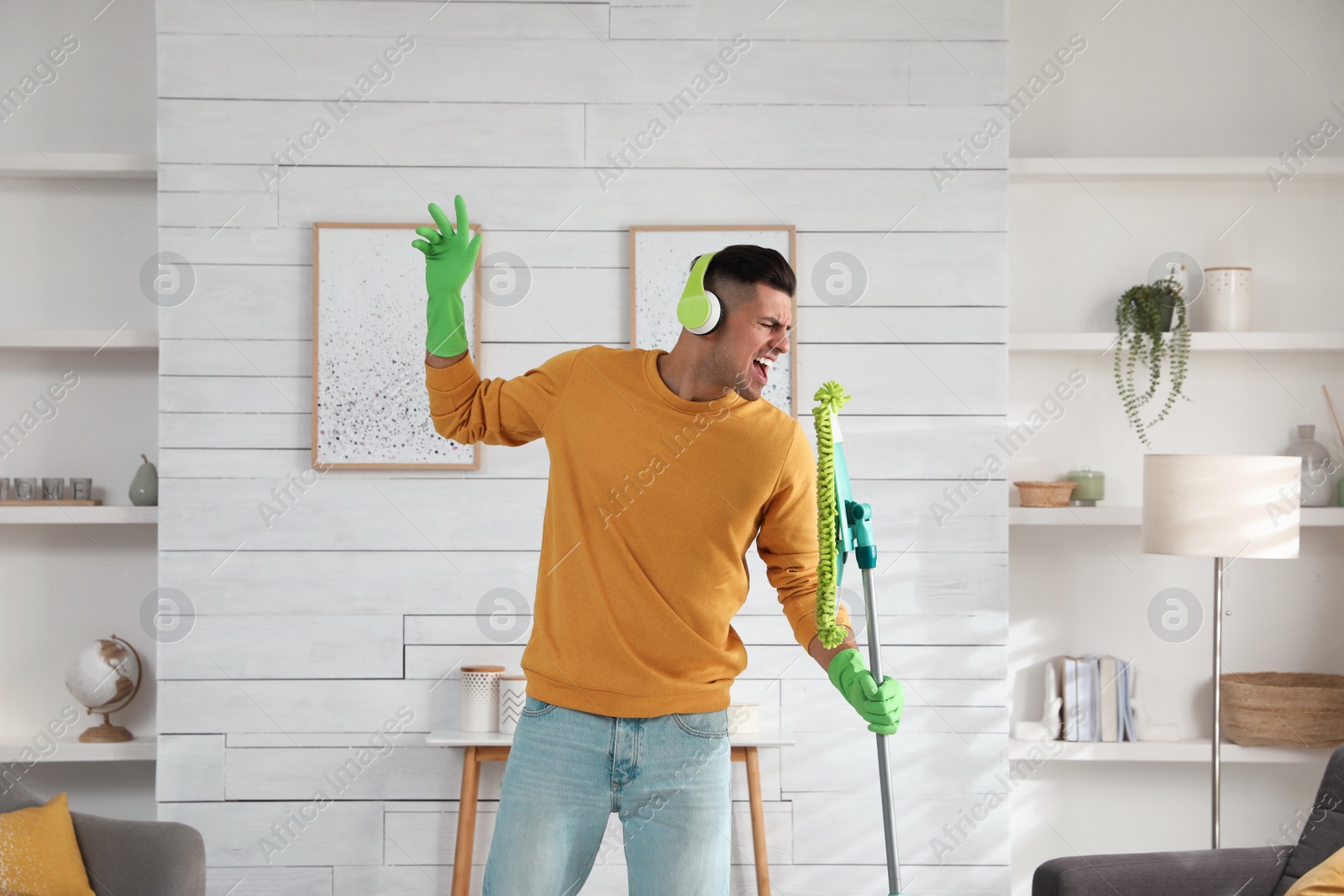 Photo of Man in headphones with mop singing while cleaning at home