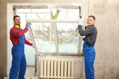 Photo of Workers in uniform installing plastic window indoors