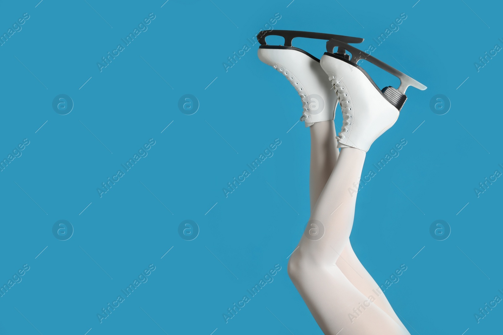 Photo of Woman in elegant white ice skates on light blue background, closeup of legs. Space for text