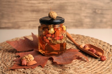 Photo of Different nuts with honey in jar, spoon and dry leaf on table