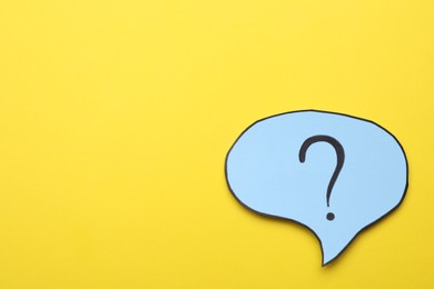 Photo of Paper speech bubble with question mark on yellow background, top view. Space for text