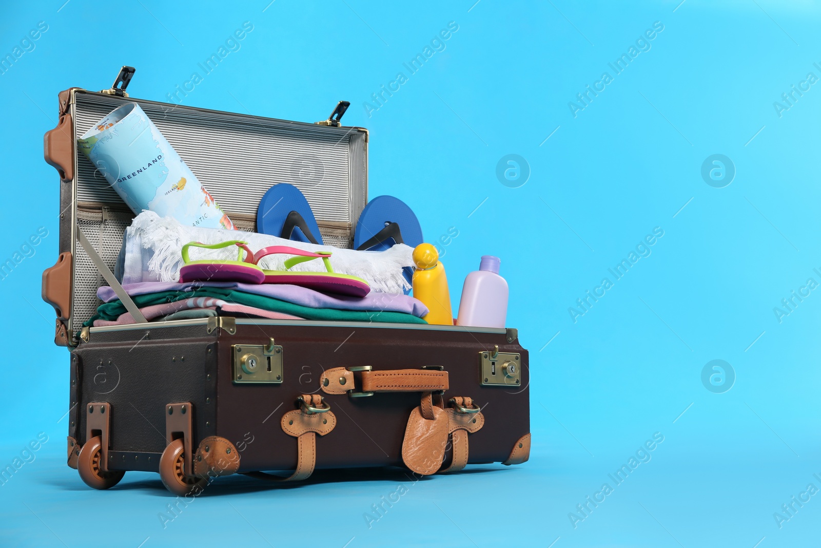 Photo of Packed vintage suitcase with different beach objects on light blue background, space for text. Summer vacation