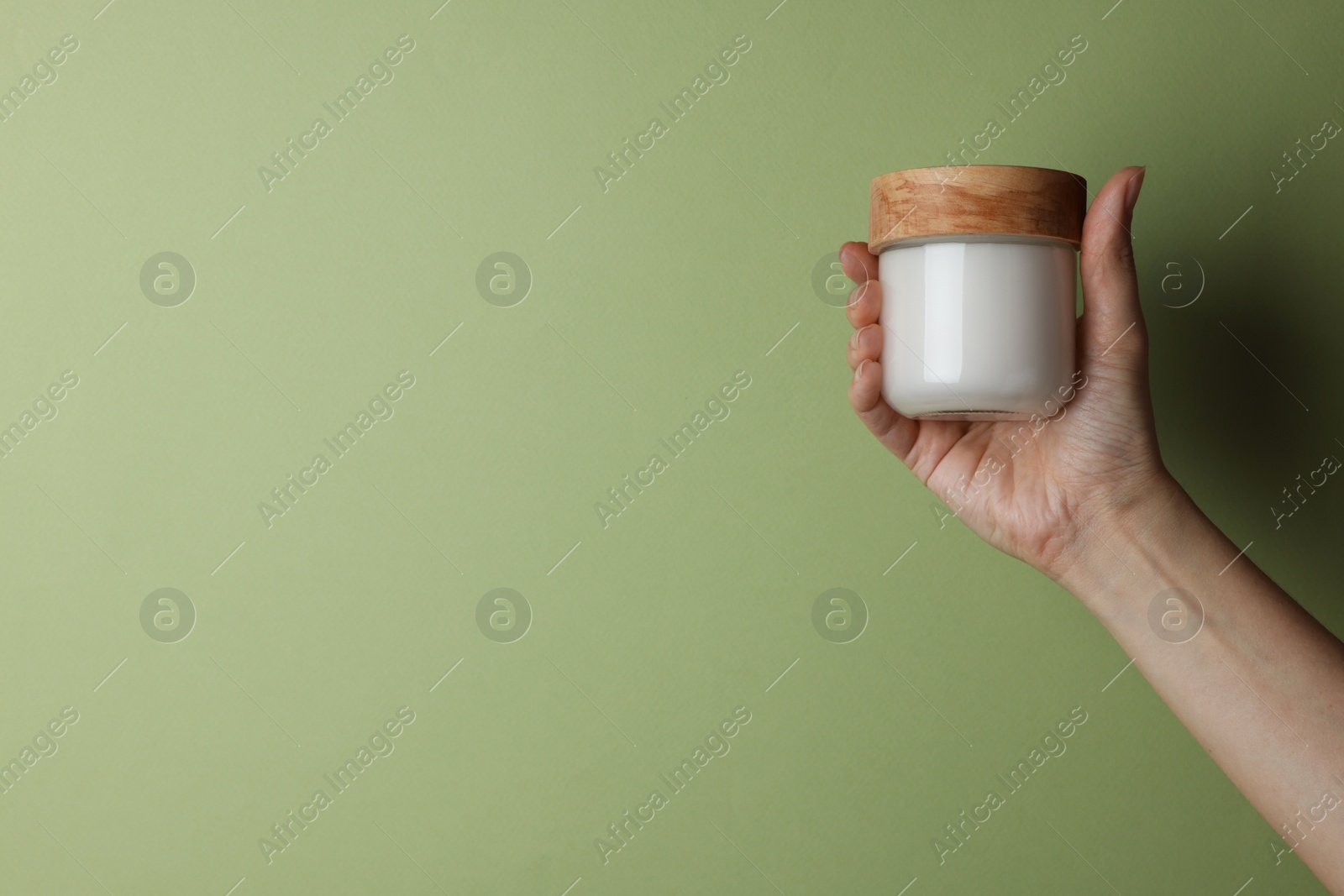 Photo of Woman holding jar of cosmetic product on pale olive background, closeup. Space for text