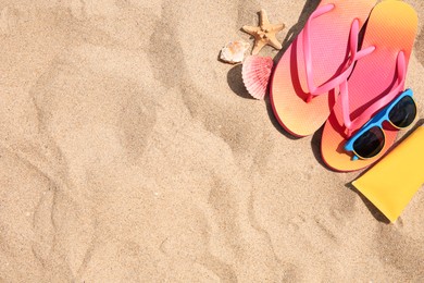 Photo of Flip flops and other beach accessories on sand, flat lay. Space for text
