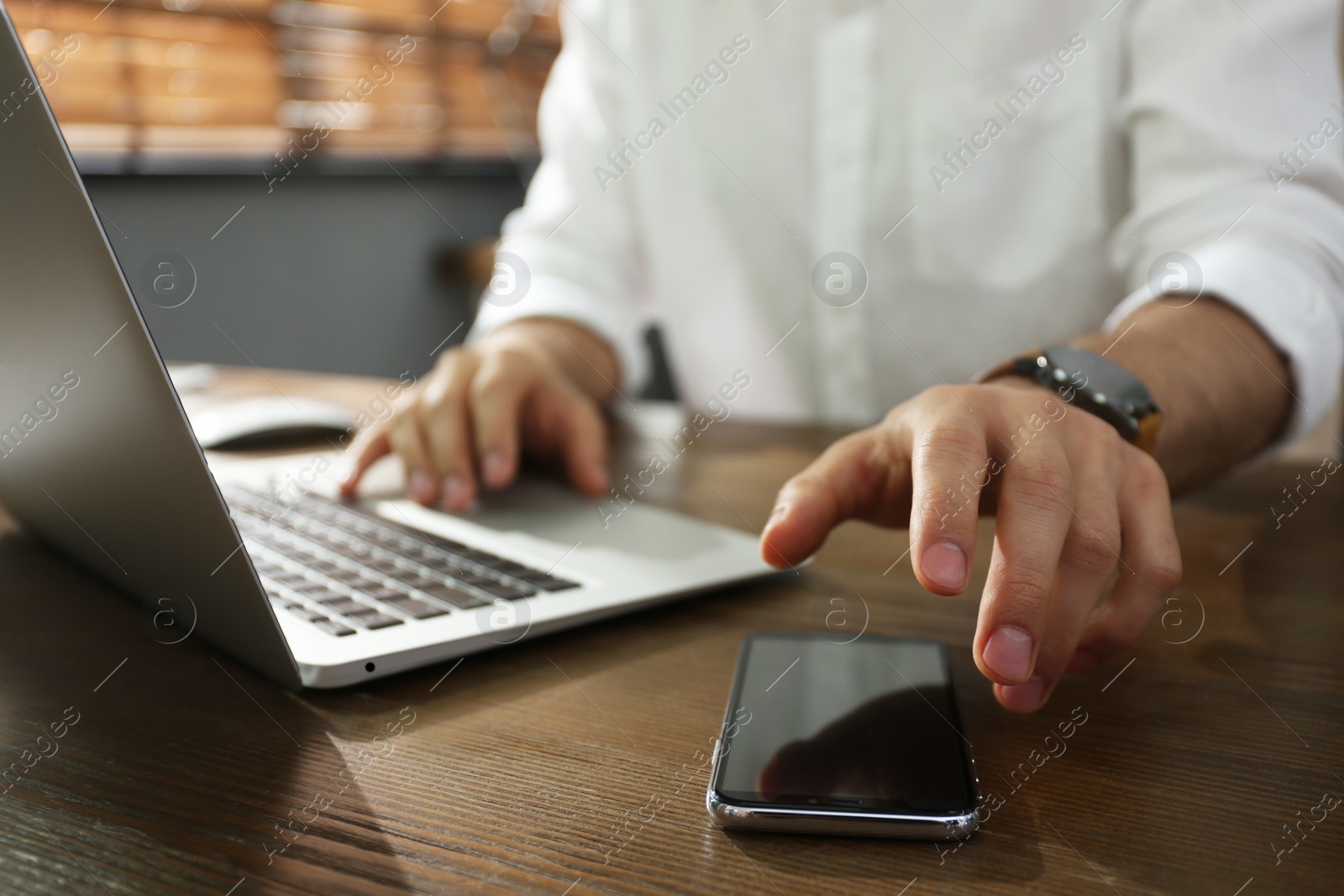 Photo of Freelancer taking smartphone while working on laptop at table indoors, closeup