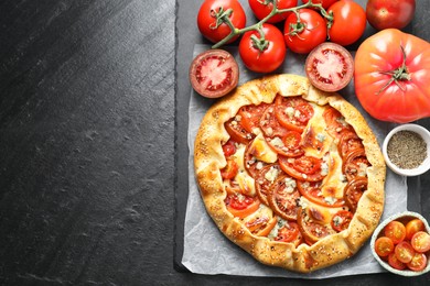 Photo of Tasty galette with tomato and cheese (Caprese galette) on dark textured table, top view. Space for text