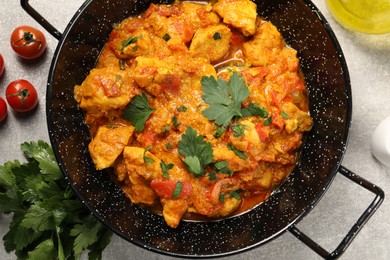 Photo of Delicious chicken curry in frying pan, parsley and tomatoes on light grey table, flat lay