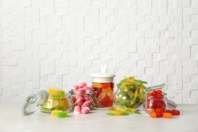 Glass jars with tasty jelly candies on table against white wall, space for text