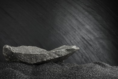 Photo of Presentation of product. Stone podium on black sand against dark textured background. Space for text