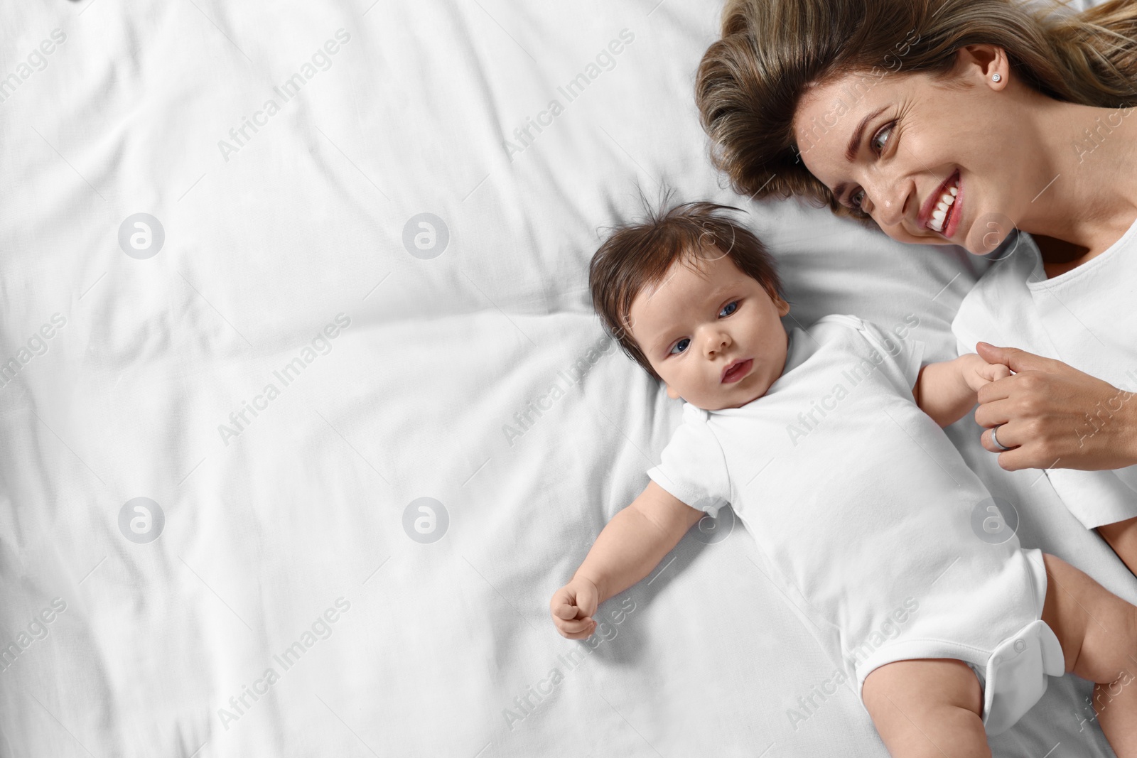 Photo of Mother and her little baby lying on bed, top view. Space for text