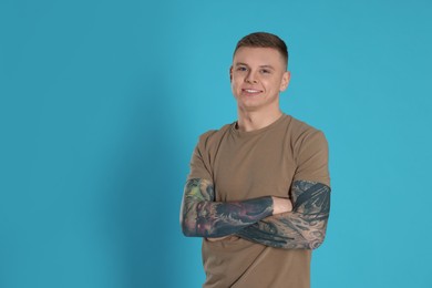 Photo of Smiling young man with tattoos on light blue background. Space for text