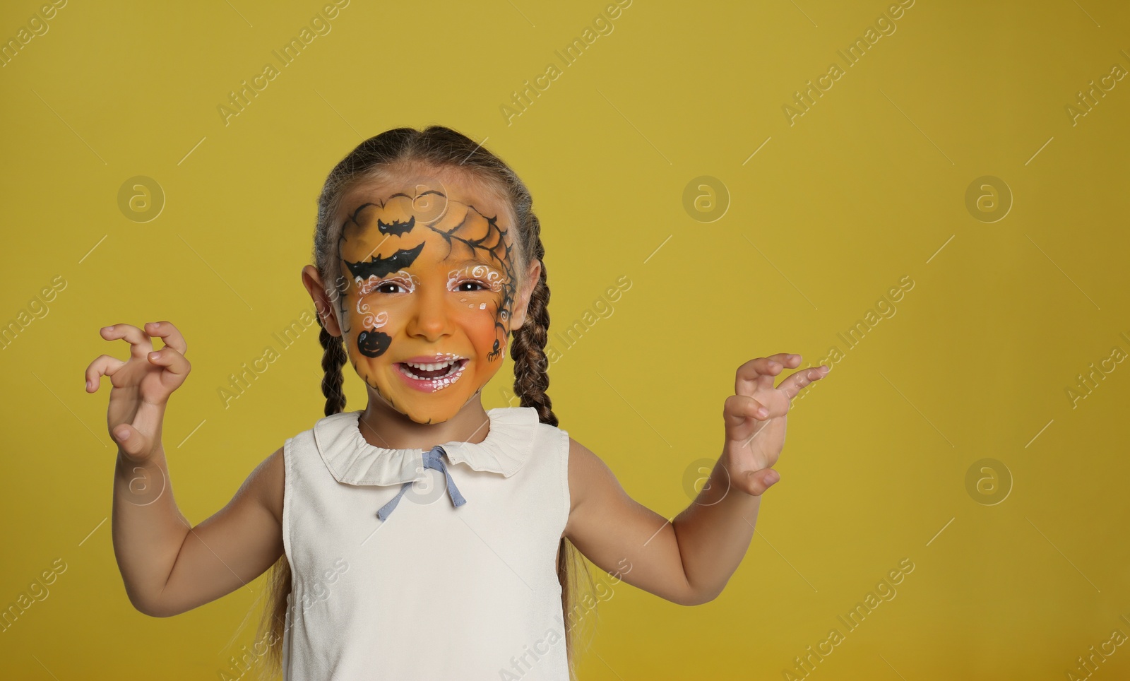 Photo of Cute little girl with face painting on orange background