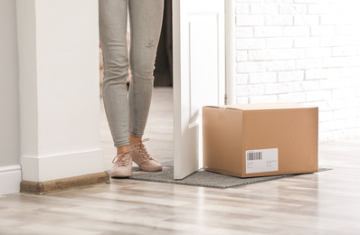 Photo of Woman in doorway and parcel on rug, closeup. Delivery service