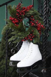 Pair of ice skates and Christmas wreath hanging on metal railing outdoors