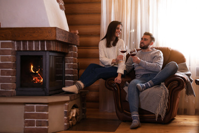 Photo of Lovely couple with glasses of wine resting near fireplace at home. Winter vacation