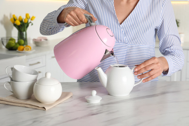 Photo of Woman pouring hot water from modern electric kettle in cup indoors, closeup