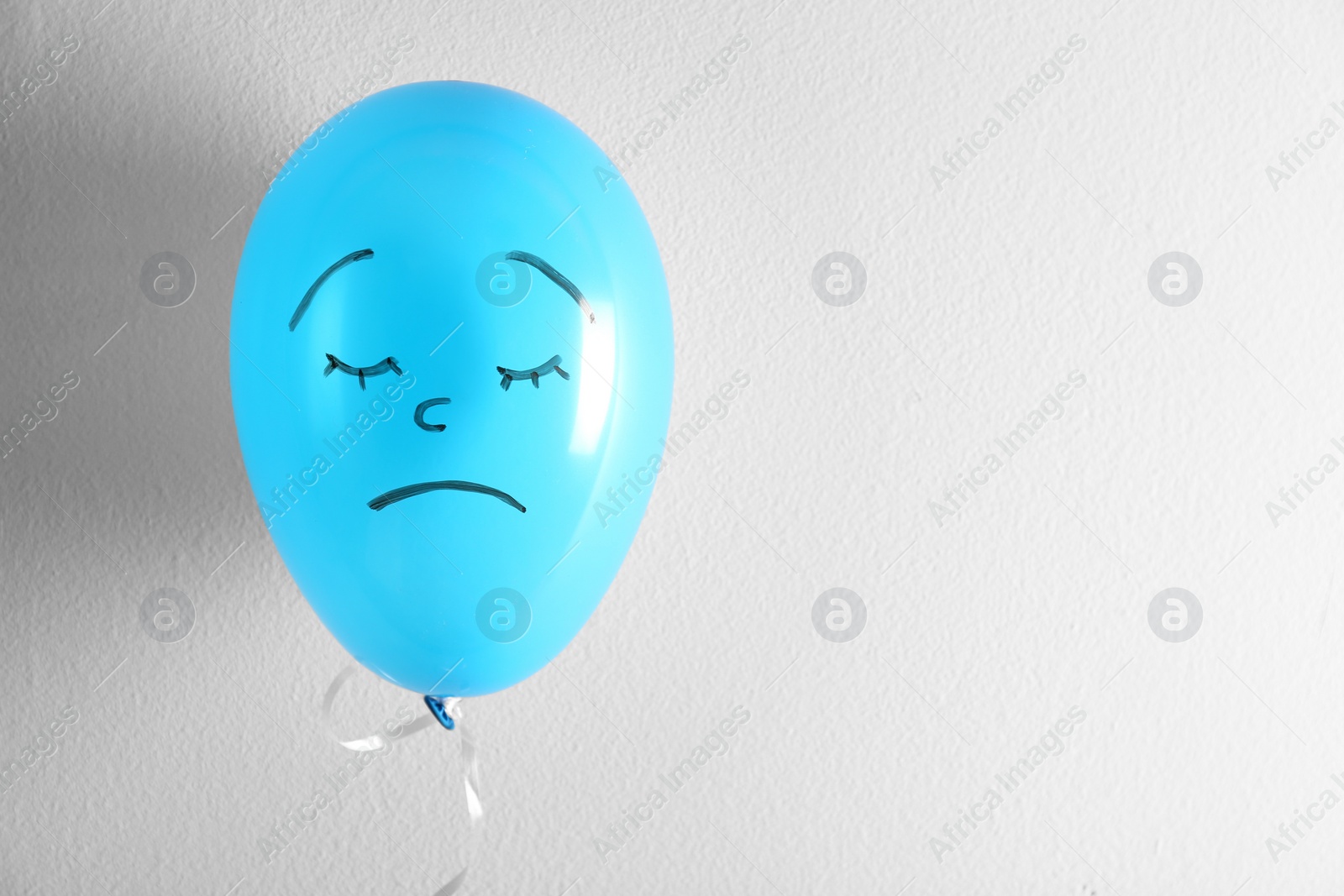 Photo of Air balloon with drawn sad face on white background. Space for text