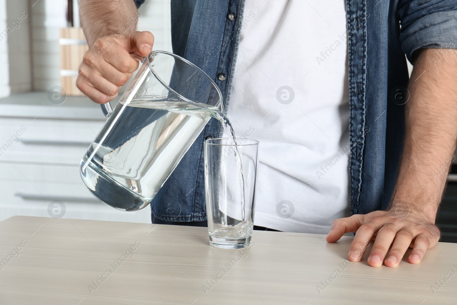 Photo of Man pouring water into glass at table, closeup