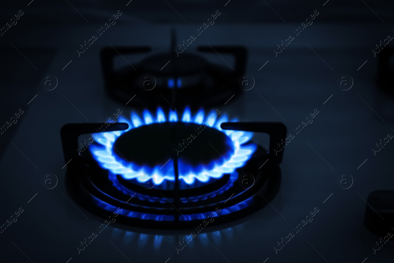 Photo of Modern gas cooktop with burning blue flame in kitchen at night