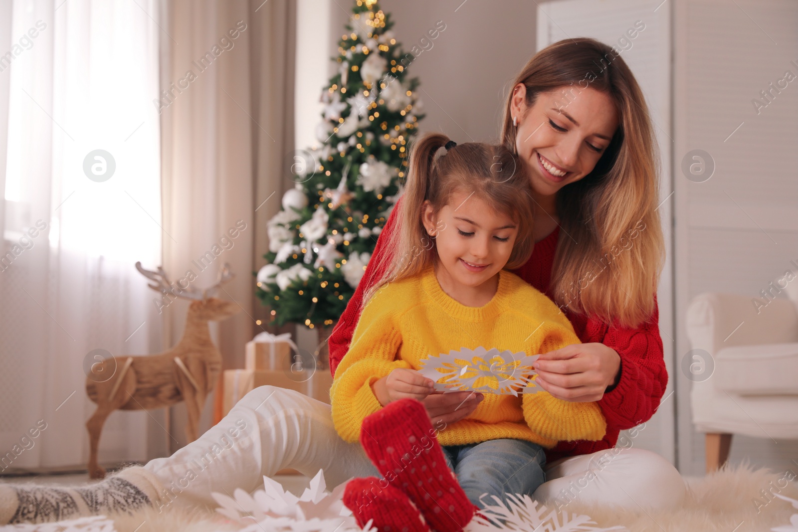 Photo of Happy mother and daughter making paper snowflake near Christmas tree at home