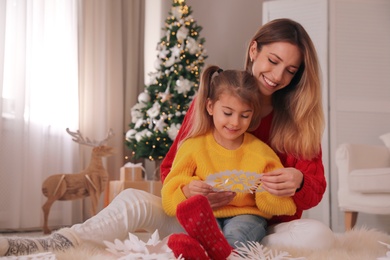 Happy mother and daughter making paper snowflake near Christmas tree at home