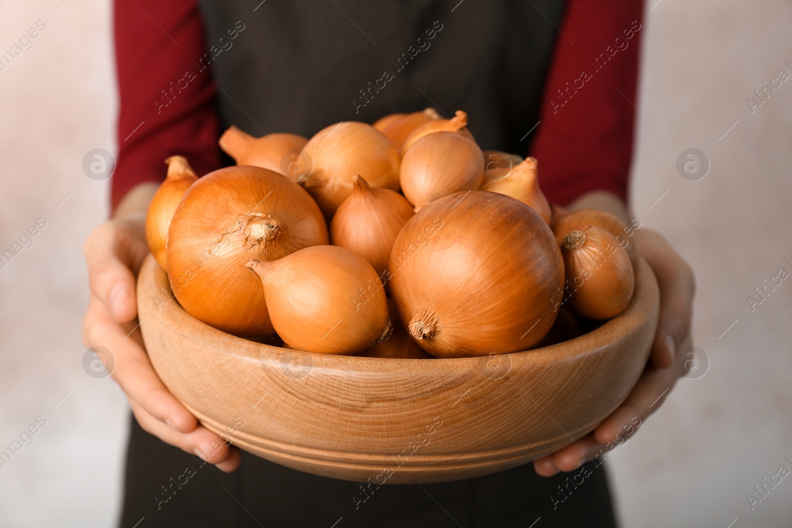 Photo of Woman holding bowl with ripe onions on grey background