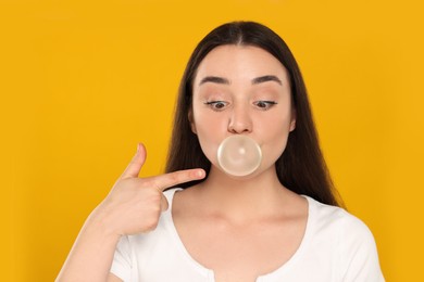 Beautiful young woman blowing bubble gum on yellow background