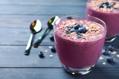 Glasses with delicious blueberry smoothie with granola on blue wooden table