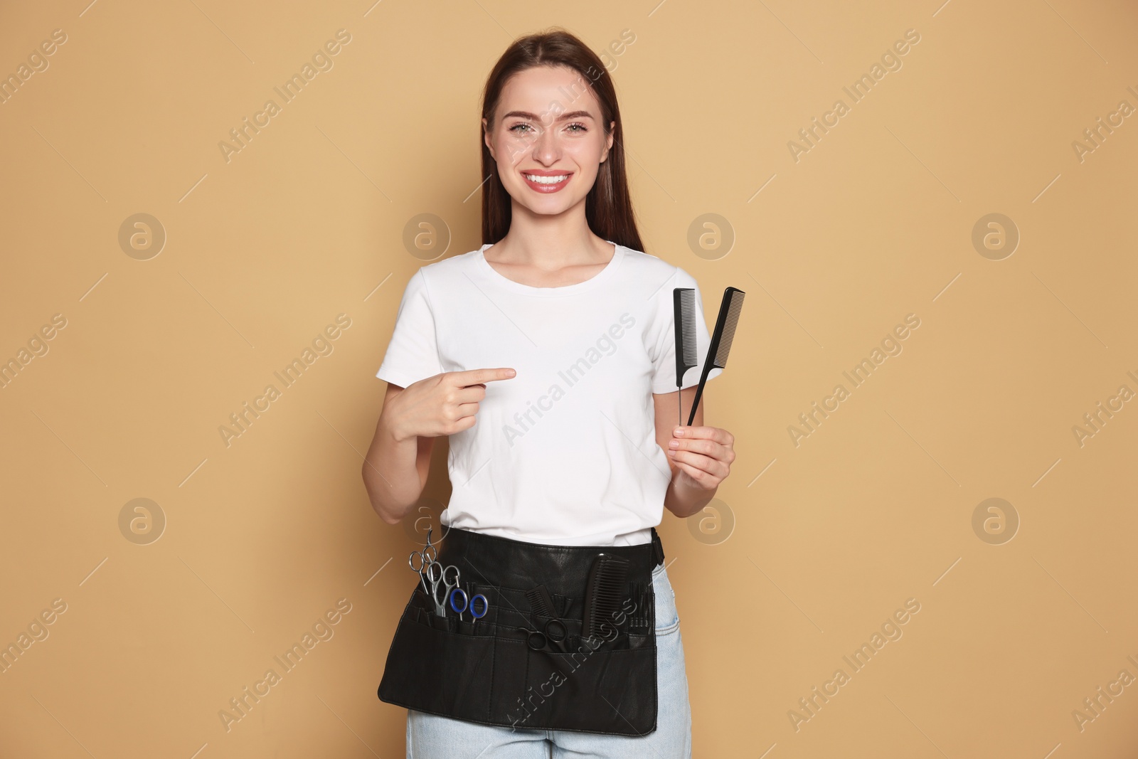 Photo of Portrait of happy hairdresser with combs on beige background