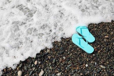 Photo of Stylish turquoise flip lops on pebble beach near beautiful sea wave, above view. Space for text