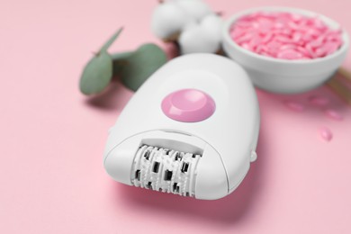 Modern epilator with depilatory wax on pink background, closeup