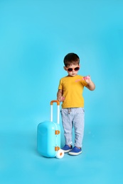 Photo of Cute little boy with sunglasses and suitcase on blue background