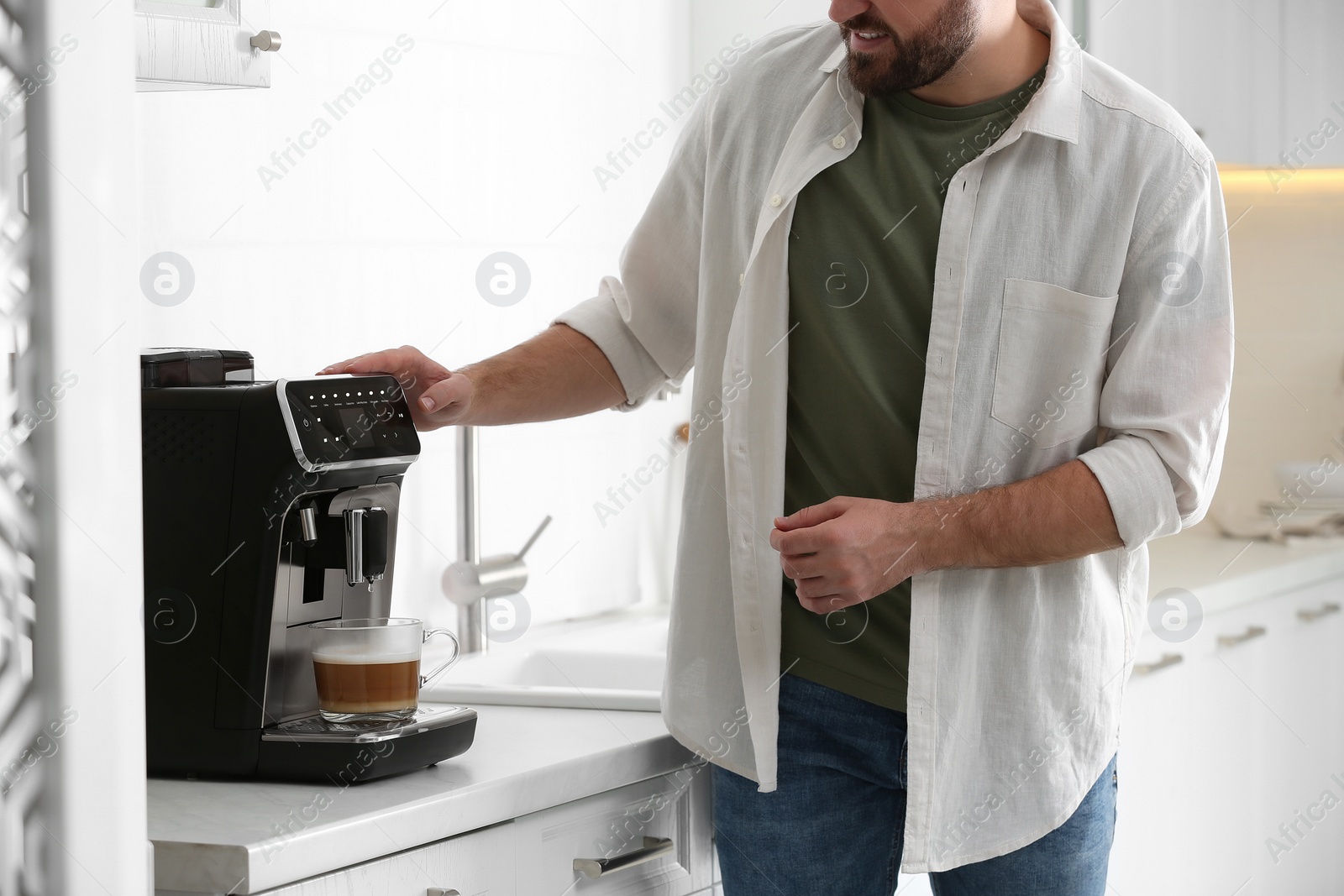 Photo of Young man preparing fresh aromatic coffee with modern machine in kitchen, closeup