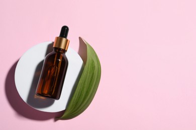 Photo of Bottle of cosmetic oil and leaf on pink background, flat lay. Space for text