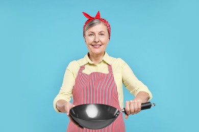 Happy housewife with frying pan on light blue background