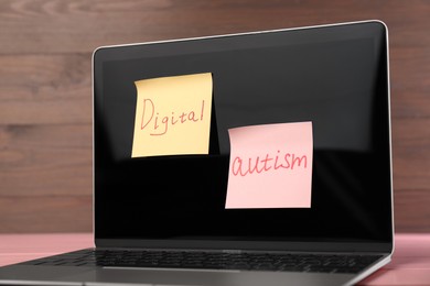 Photo of Sticky notes with phrase Digital Autism attached to laptop on table, closeup. Addictive behavior