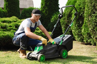 Photo of Young man with screwdriver fixing lawn mower in garden on sunny day