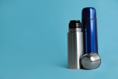 Stylish thermo bottles on light blue background, space for text