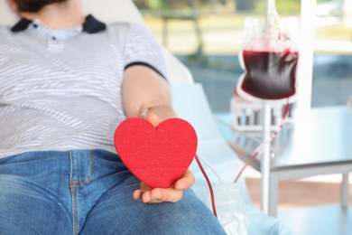 Photo of Man holding heart while making blood donation at hospital, closeup