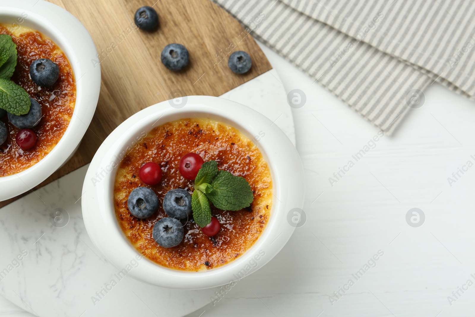 Photo of Delicious creme brulee with berries and mint in bowls on white wooden table, top view. Space for text